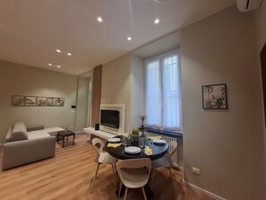 Una sala moderna con un sofá, una mesa de comedor para dos personas y un televisor montado en la pared.