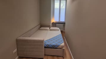 Una habitación pequeña con una cama, un banco, un radiador y una ventana.