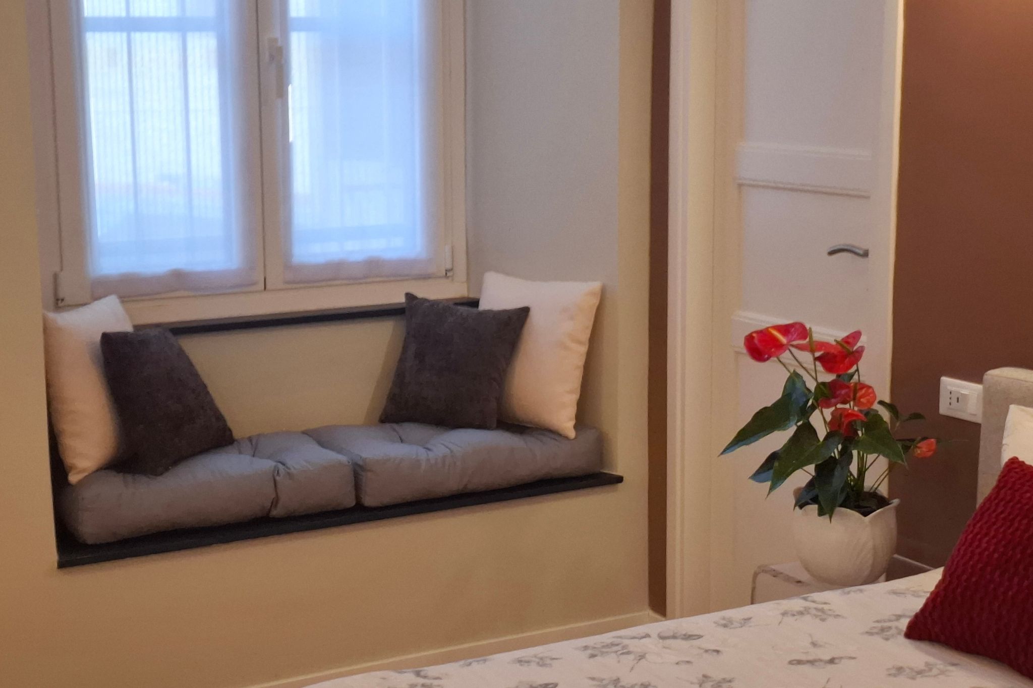 Une pièce avec un banc intégré le long du mur, une plante en pot avec des fleurs rouges et un lit avec une tête de lit blanche.