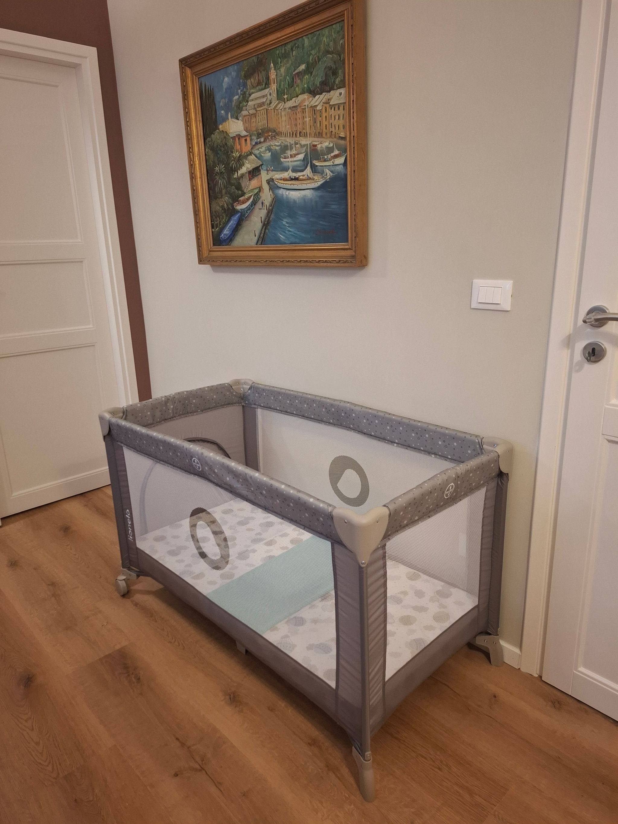 Un parc pour bébé avec un matelas à motifs, une porte et un tableau accroché au mur.