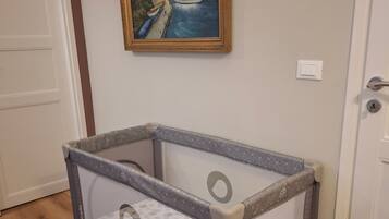 A baby playpen with a patterned mattress, a door, and a painting on the wall.
