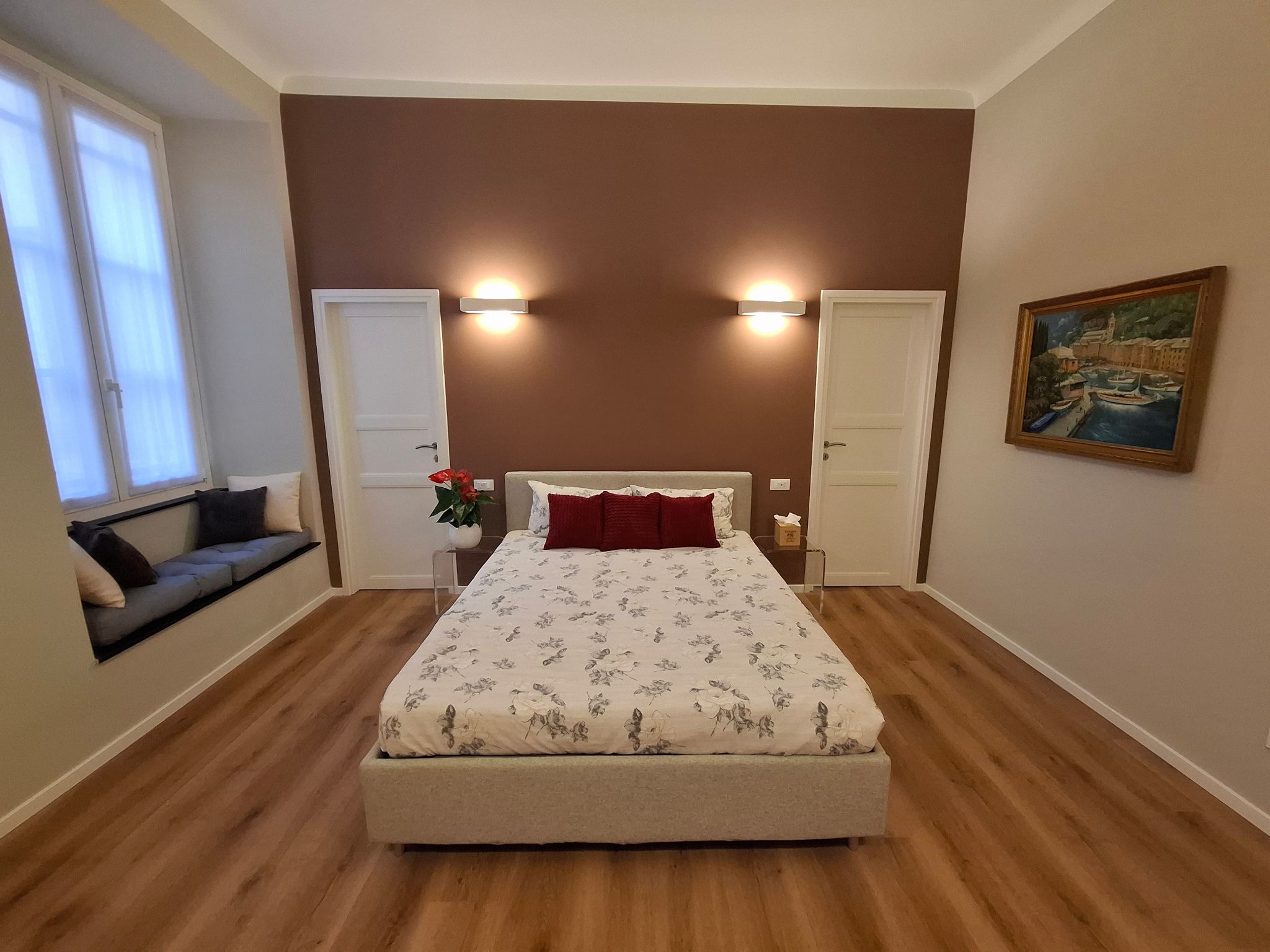 Un dormitorio con cama, dos puertas, una ventana, un cuadro y una planta.