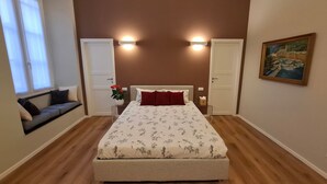 Een slaapkamer met een bed, twee deuren, een raam, een schilderij en een plant.