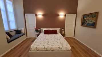 Un dormitorio con cama, dos puertas, una ventana, un cuadro y una planta.