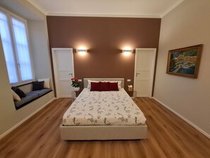Un dormitorio con cama, dos puertas, una ventana, un cuadro y una planta.
