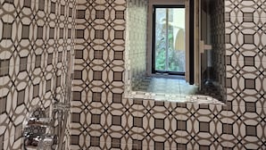 Een badkamer met een betegelde vloer in geometrisch patroon, een douche met een moderne kraan en een raam met uitzicht op groen.