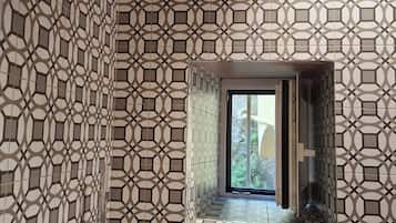 Un baño con diseño de baldosas geométricas, una ducha con grifería moderna y una ventana con vista a follaje.