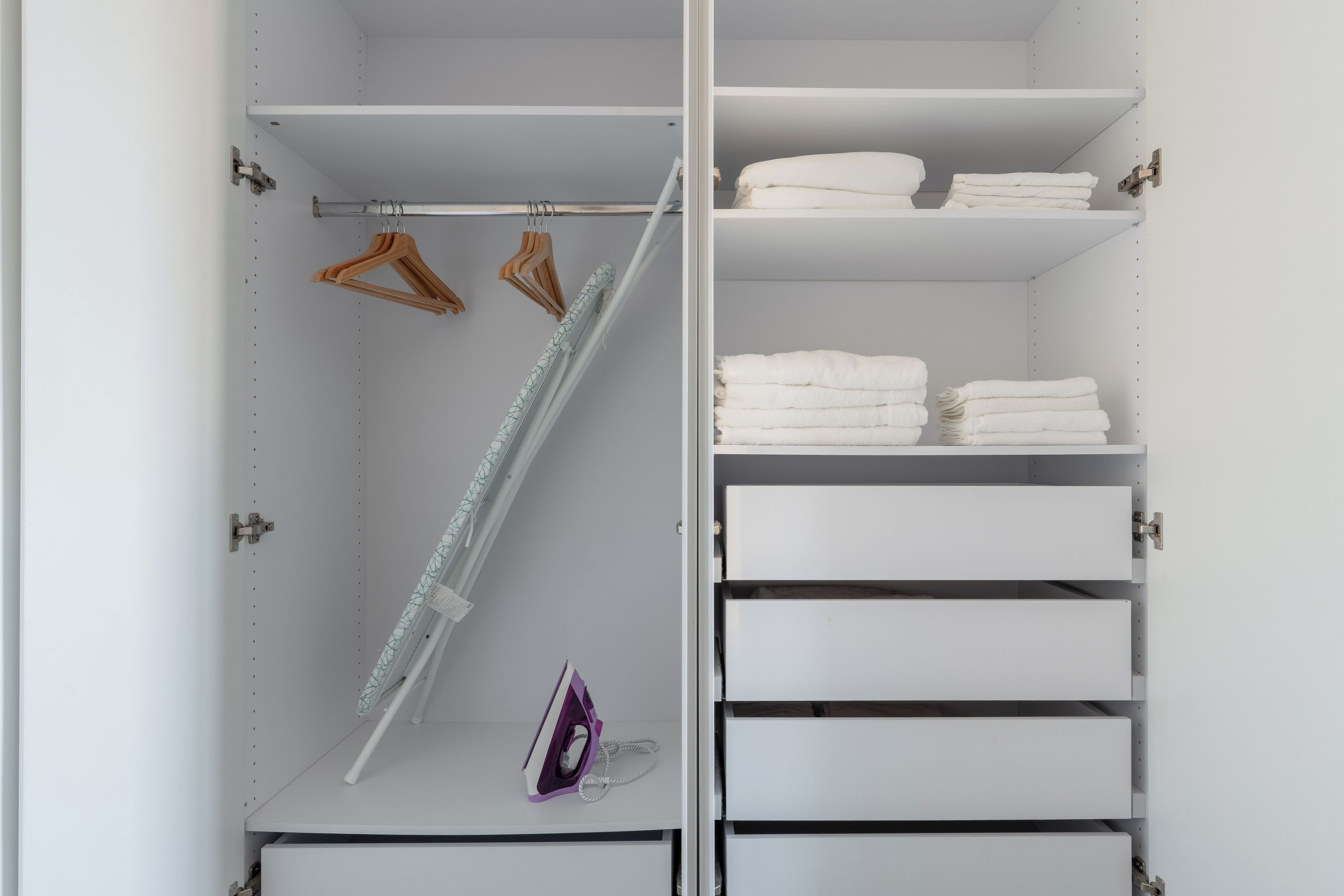 A closet with white shelves, wooden hangers, and a hanging rod.