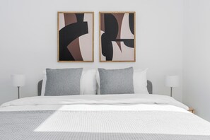 Un dormitori modern amb un llit gran, dos almoinos i una obra d'art abstracta a la paret.