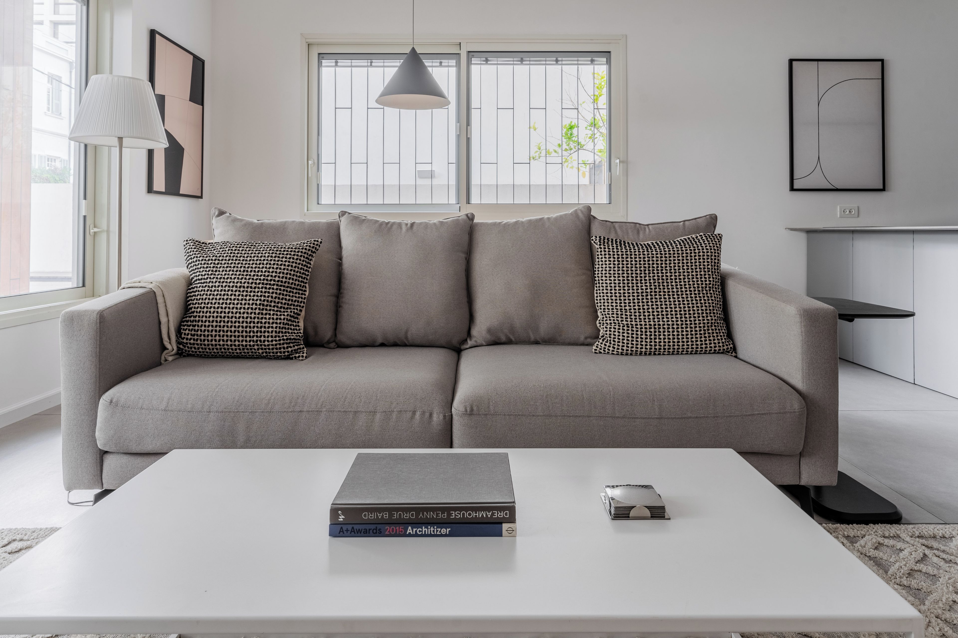 A modern living room with a grey sofa, patterned cushions, a white coffee table, and books.