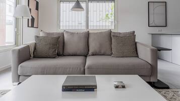 A modern living room with a grey sofa, patterned cushions, a white coffee table, and books.