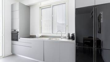 A modern kitchen with a built-in oven, a sink, and a window with blinds.