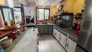 A kitchen with white cabinets, a stainless steel refrigerator, and a window with a view of greenery. - Beautiful vacation villa 🌴 (Le Tampon)