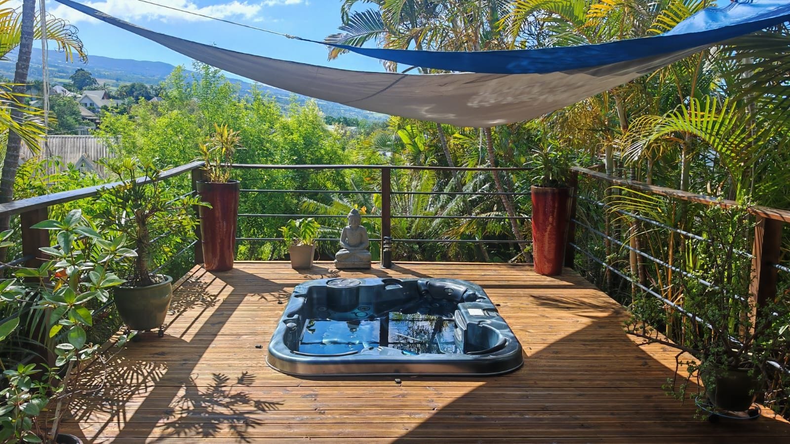 A hot tub on a wooden deck with a view of a lush garden and distant hills.