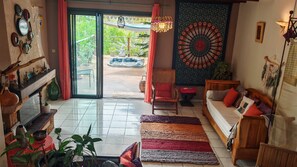 A cozy living room with a sofa, a chair, a fireplace, and a view of a garden through a glass door. - Beautiful vacation villa 🌴 (Le Tampon)
