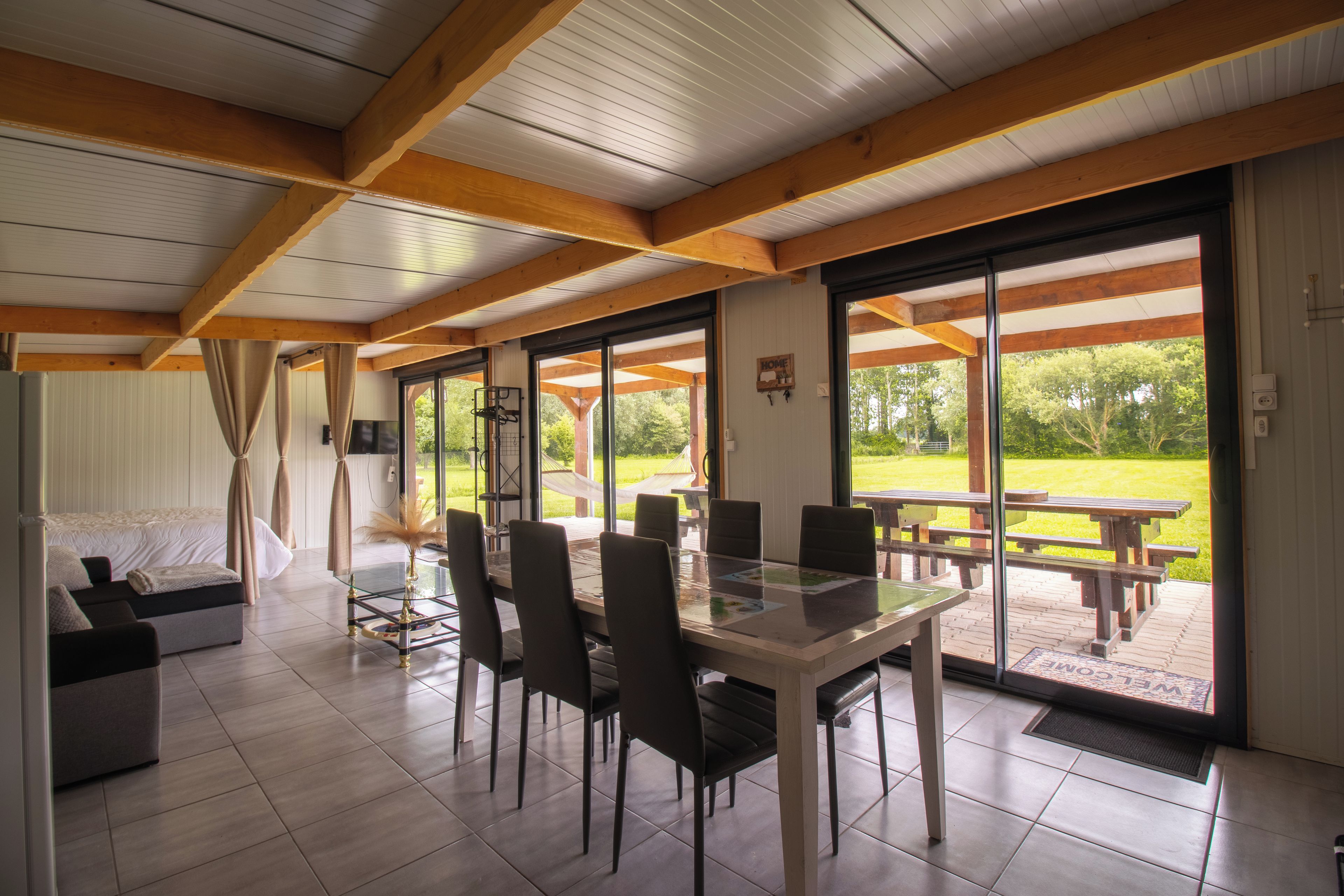 Un coin repas avec une table et des chaises en verre, un canapé et une vue sur un jardin grâce à de grandes fenêtres.