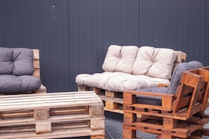 Eine Holzbank und ein aus Paletten gefertigtes Sofa, platziert vor einer dunklen Wand.