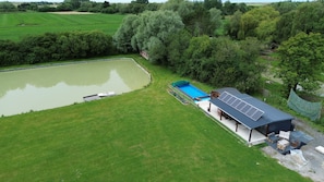 Ein großes, grünes Feld mit einem Schwimmbad, einer überdachten Sitzgelegenheit im Freien und einem kleinen Boot, das am Wasser liegt.