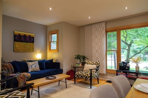 A living room with a blue sofa, a wooden coffee table, a patterned armchair, and a view of greenery outside. - Charming Saugatuck retreat less than a mile from downtown with nature preserve views. (Saugatuck)