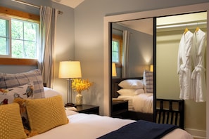 A hotel room with a bed, a bedside lamp, a vase with flowers, a mirror, and a wardrobe with hanging robes. - Charming Saugatuck retreat less than a mile from downtown with nature preserve views. (Saugatuck)