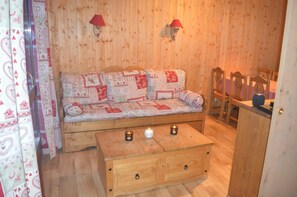 Et hyggeligt rum med en træsofa, en trækiste og to vægmonterede lamper.