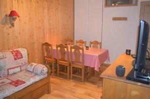A cozy room with a wooden floor, a checkered table, wooden chairs, a sofa with a quilt, a lamp, and a television. - Apartment for 6 People in Valmeinier (Valmeinier)