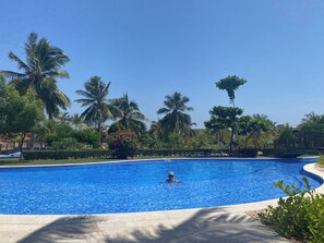 Ein Schwimmbecken mit einer Person im Wasser, umgeben von Palmen und blauem Himmel.