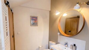 Un bany amb un lavabo de fusta, un mirall rodó i un vàter.