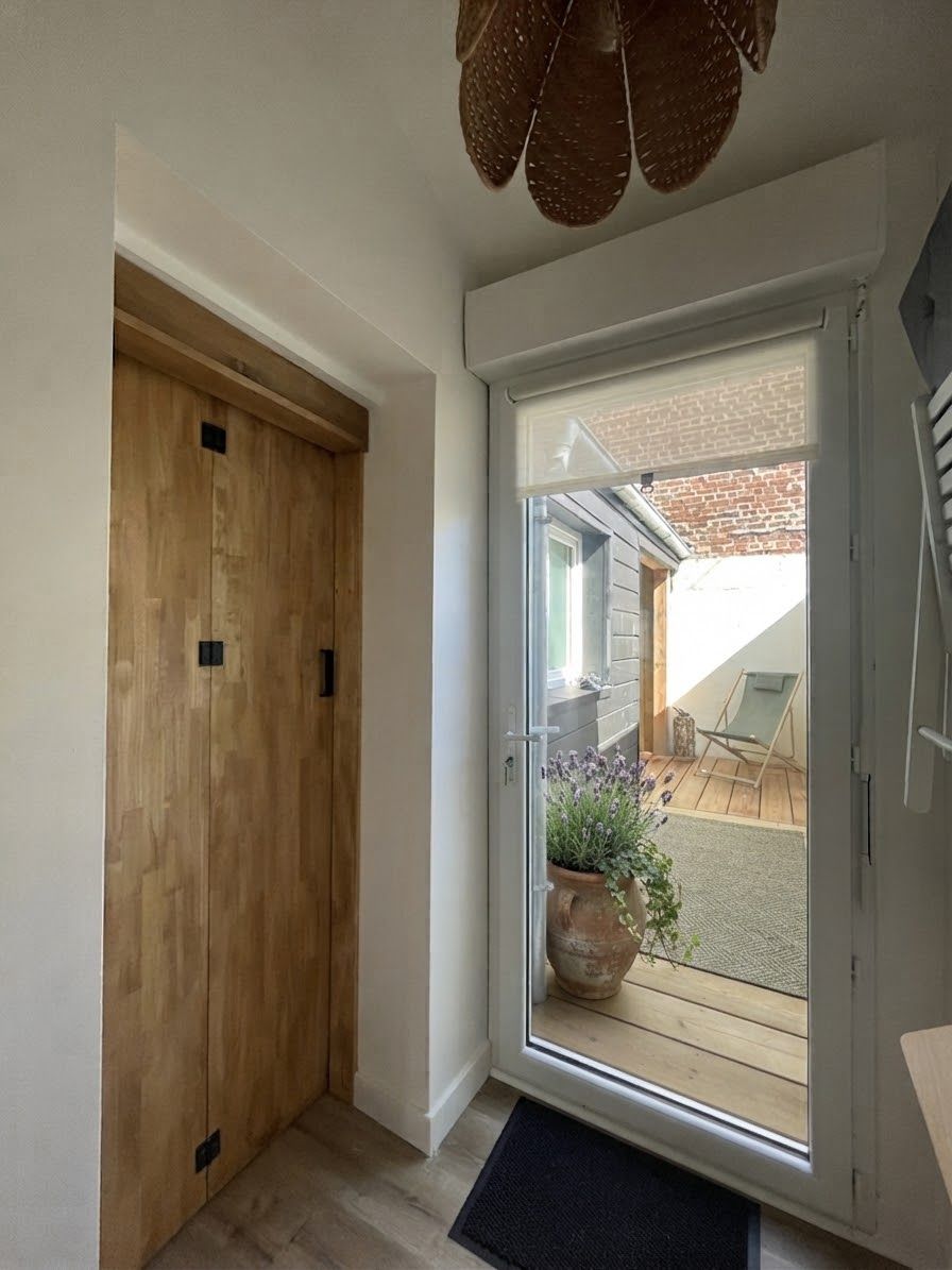 Une porte en bois donnant sur un balcon où se trouvent un pot de fleurs et une chaise.