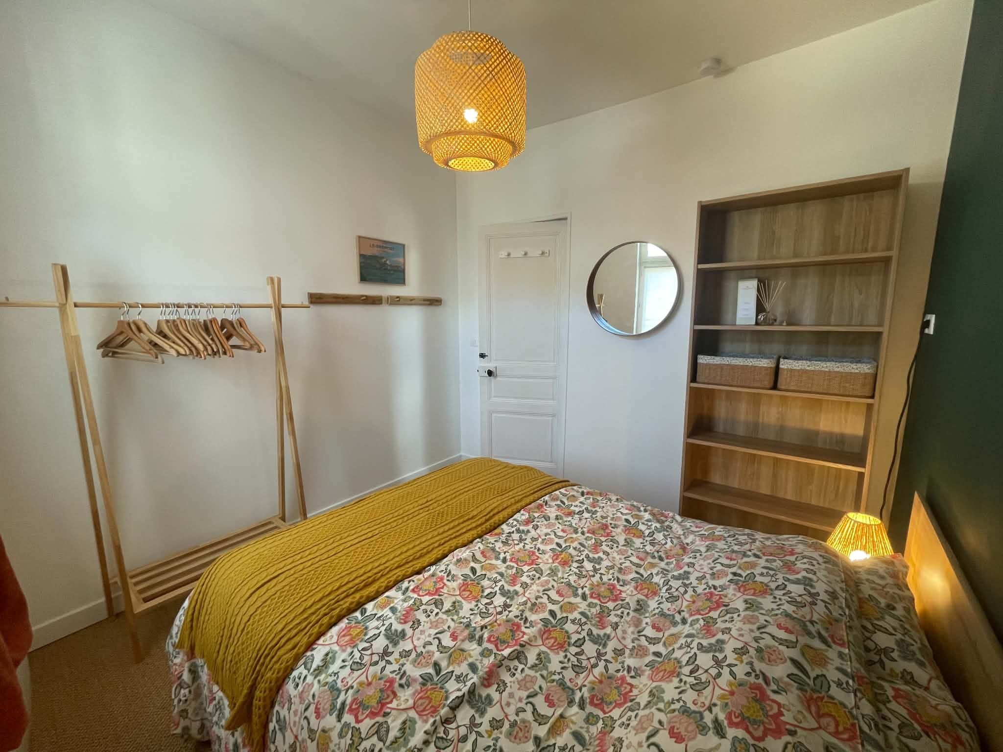 Une chambre à coucher comprenant un lit, une armoire en bois, un miroir et un luminaire suspendu.