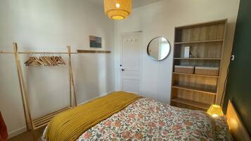 Une chambre à coucher comprenant un lit, une armoire en bois, un miroir et un luminaire suspendu.