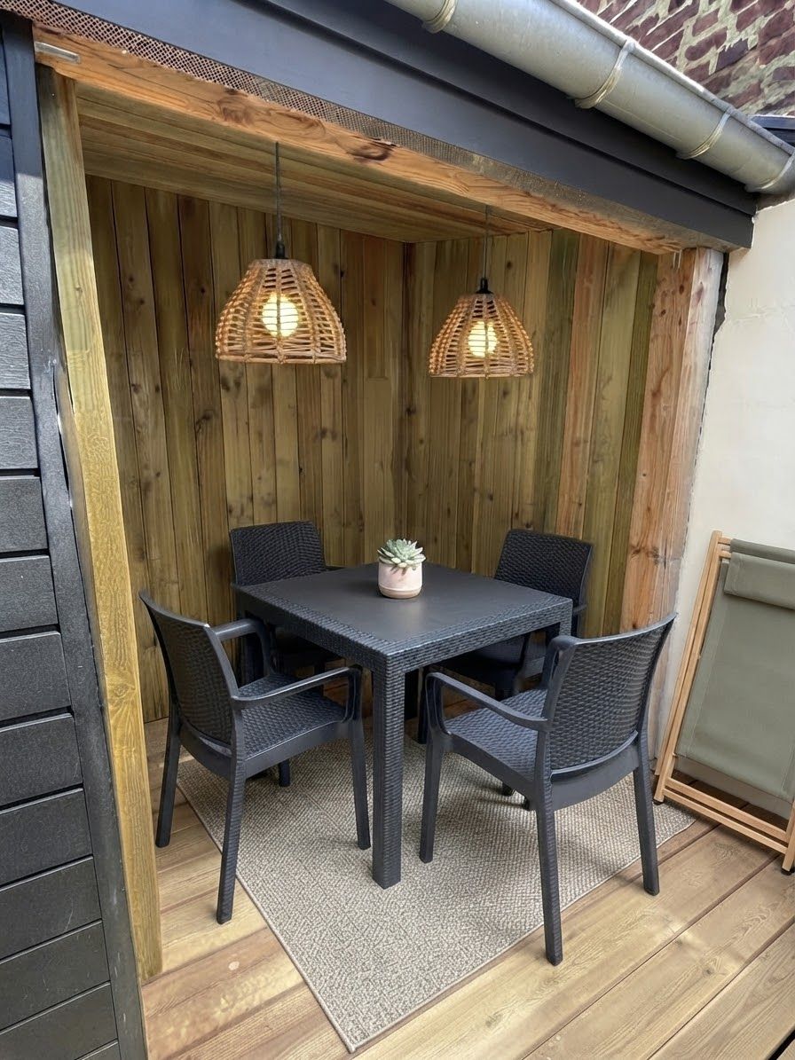 Un coin repas comprenant une table et des chaises, deux lampes suspendues et une petite plante posée sur la table.