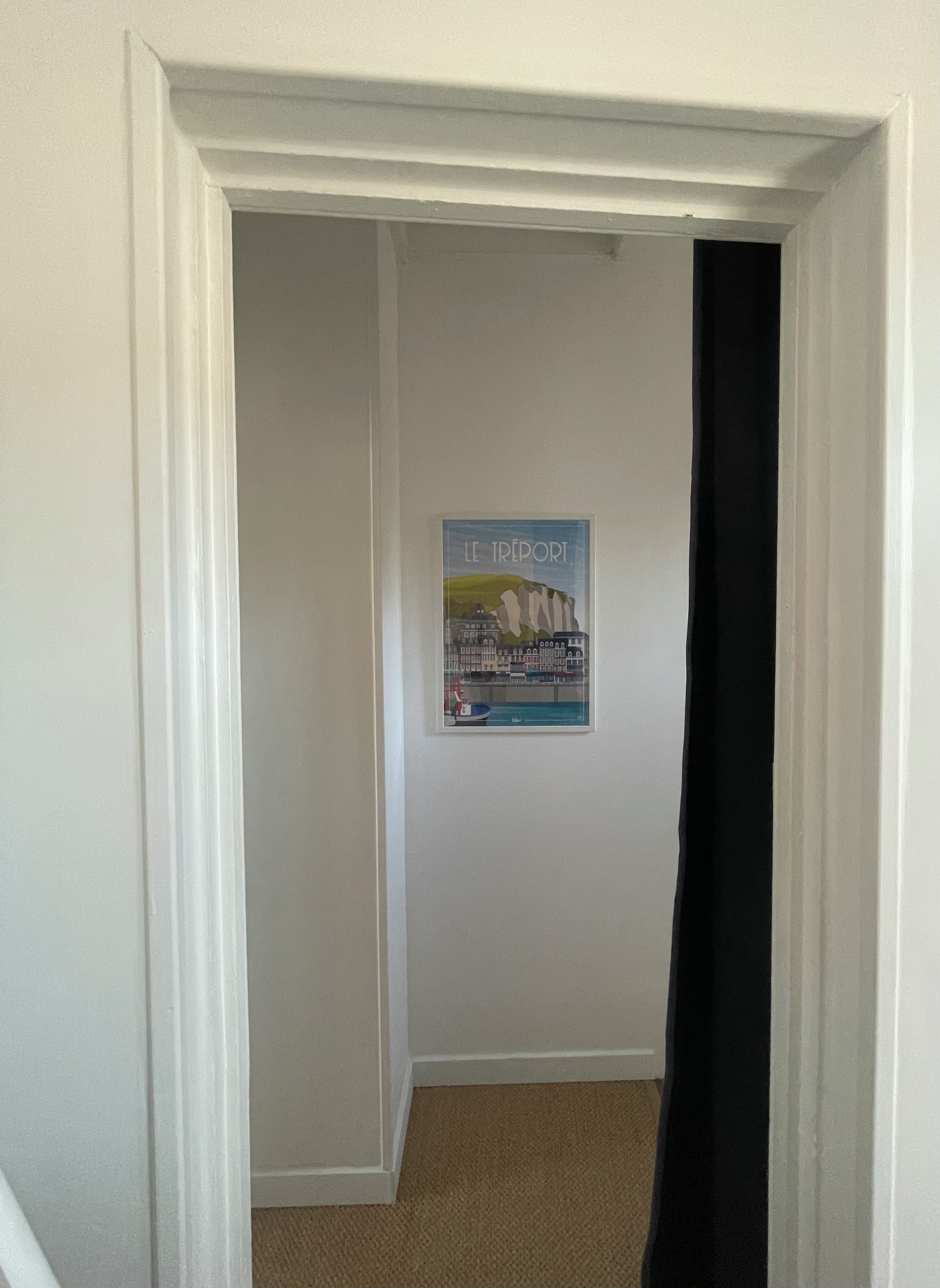 Un couloir avec une affiche encadrée accrochée au mur et un rideau noir qui recouvre partiellement l’entrée.