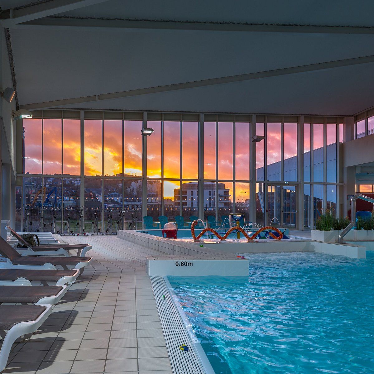 An indoor swimming pool with a sunset view, lounge chairs, and a lifeguard stand.