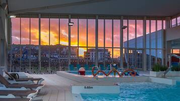 An indoor swimming pool with a sunset view, lounge chairs, and a lifeguard stand.