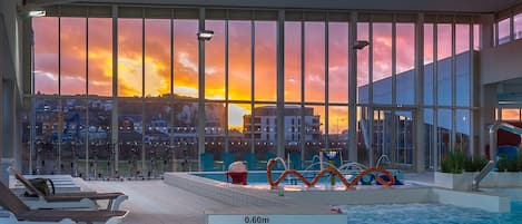 An indoor swimming pool with a sunset view, lounge chairs, and a lifeguard stand.