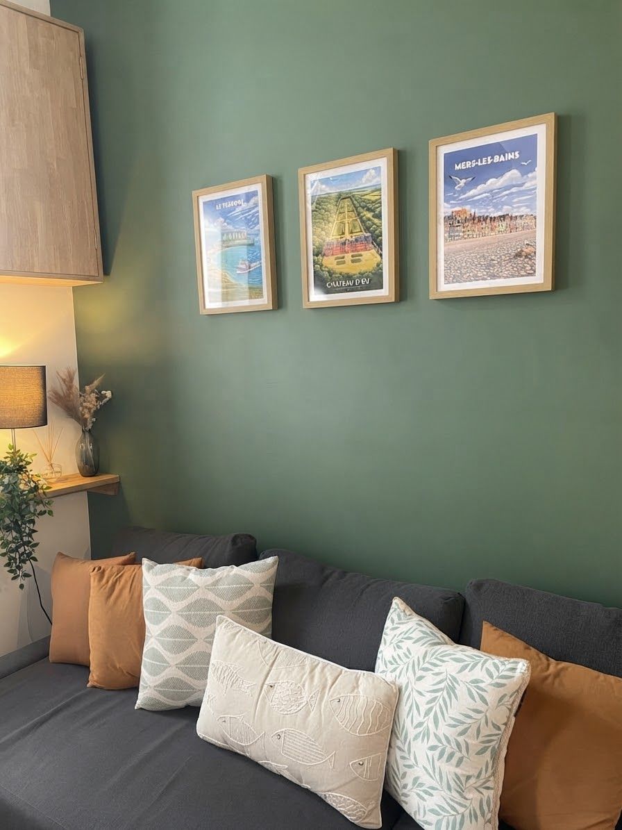 Une pièce avec un mur vert, un canapé agrémenté de coussins à motifs et trois tableaux encadrés.