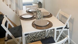 Zona de menjador amb taula blanca preparada per a quatre, incloent plats, coberts i una gerra.