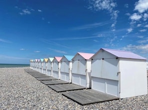 A row of beach huts with a wooden deck in front, set on a pebbled beach with a clear sky. - Fully renovated Les Tamaris house, with all modern amenities, featuring a courtyard and Wi-Fi (Le Tréport)