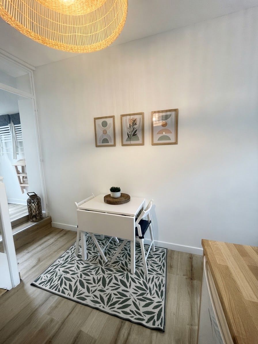 A clean, modern room with a white table, a chair, and a patterned rug. There are three framed pictures on the wall.