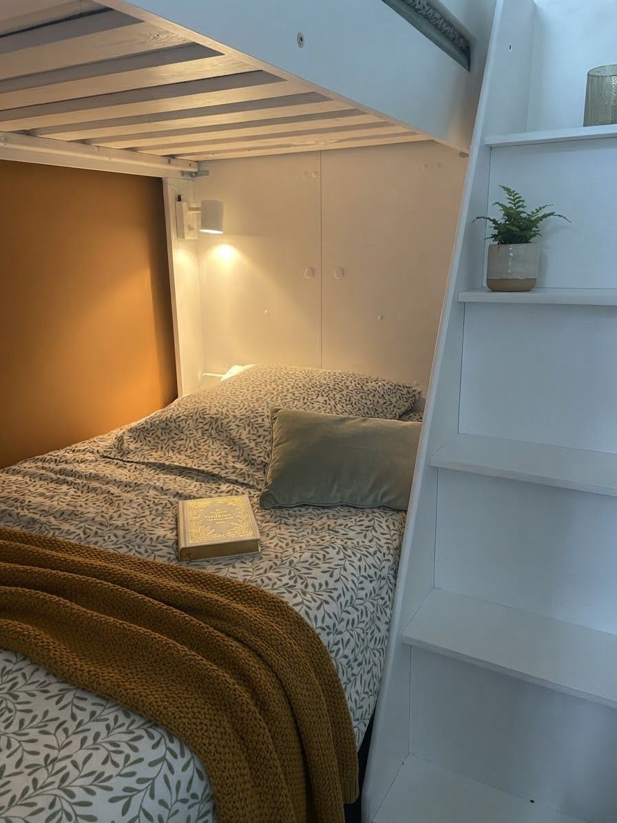 Un lit superposé avec une tête de lit, une table de chevet avec une lampe et une petite plante en pot posée sur une étagère.