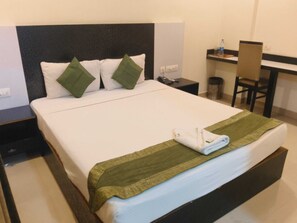 A hotel room with a bed, a desk, a chair, and a trash bin. - Townhouse Technopark Phase 1 (Thiruvananthapuram)