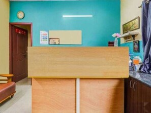 A reception area with a wooden desk, a clock on the wall, and a door to the left. - Townhouse Technopark Phase 1 (Thiruvananthapuram)