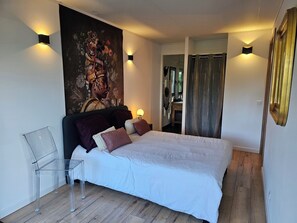 Ein Schlafzimmer mit einem Bett, Nachttischlampen, einem klaren Glasstuhl, einem großen Wandteppich und einem Spiegel.