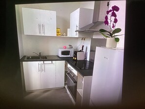 A compact kitchen with white cabinets, a microwave, a sink, and a small refrigerator. - Apartment in the heart of the village, in a quiet location, with a panoramic view. (Forcalquier)