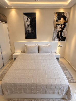 A bedroom with a large bed, two bedside tables, and artwork on the walls. - APARTMENT 3 MINUTES FROM THE AIRPORT (marrakech)