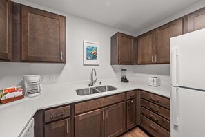 Eine Küche mit Holzausstattung, einer weißen Arbeitsplatte, einem Spülbecken, einer Kaffeemaschine, einem Toaster und einem Kühlschrank.