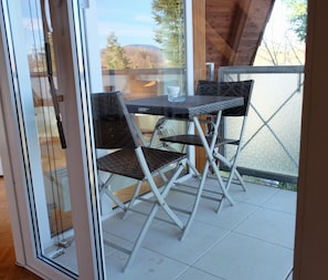 Eine Glastür führt zu einem Sitzbereich im Freien mit einem Tisch und zwei Stühlen.