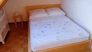 A single bed with a patterned bedspread, a bedside table with a lamp, and a small round table. - Vrbo Property (Freiburg im Breisgau)