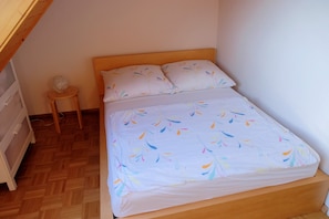 Ein Einzelbett mit einem gemusterten Überwurf, ein Nachttisch mit Lampe und ein kleiner runder Tisch.